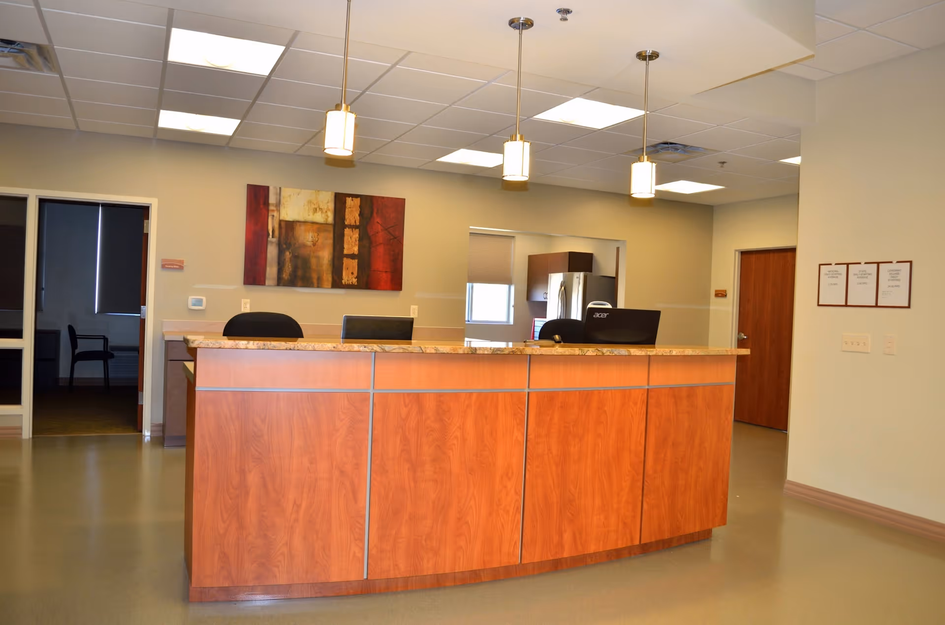 A reception desk area with a curved wooden front desk, pendant lights, wall artwork and adjacent office doors.