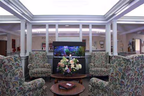 A TV lounge area with floral chairs around a coffee table in a bright facility lobby.