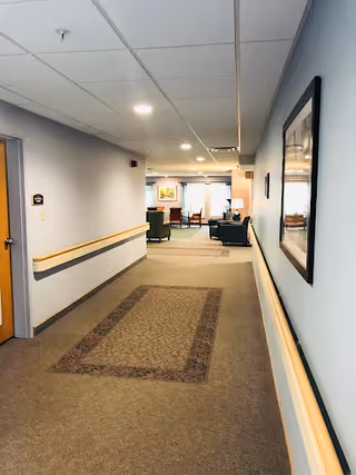 Interior corridor with handrails, carpet runner, ceiling lights and a seating area visible at the far end.