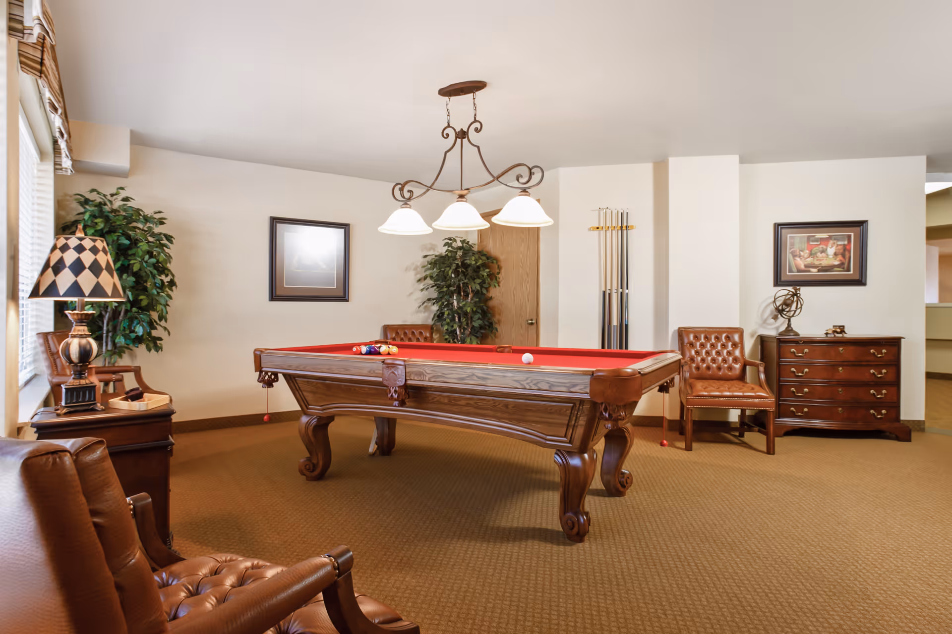 Interior recreation room with a red-felt pool table, leather chairs, framed artwork, and lamps.