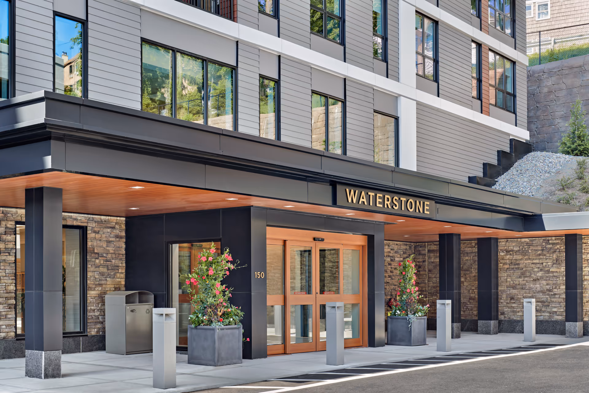Modern building entrance with a covered porte-cochere and a 'WATERSTONE' sign above the glass doors.