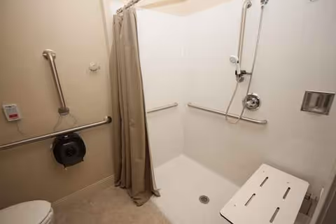 Accessible bathroom with walk-in shower, grab bars, and folding chair.