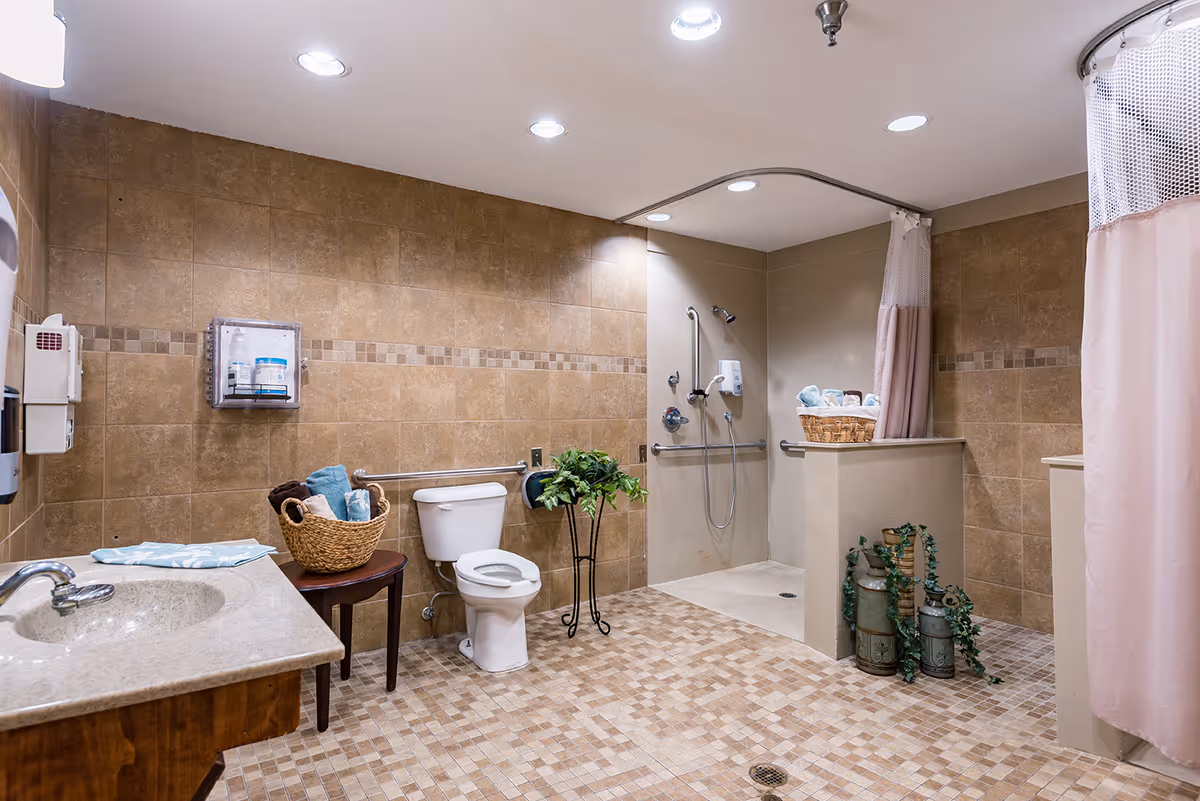 Accessible tiled bathroom with a walk-in shower, toilet, sink vanity, grab bars, and decorative baskets and plants.