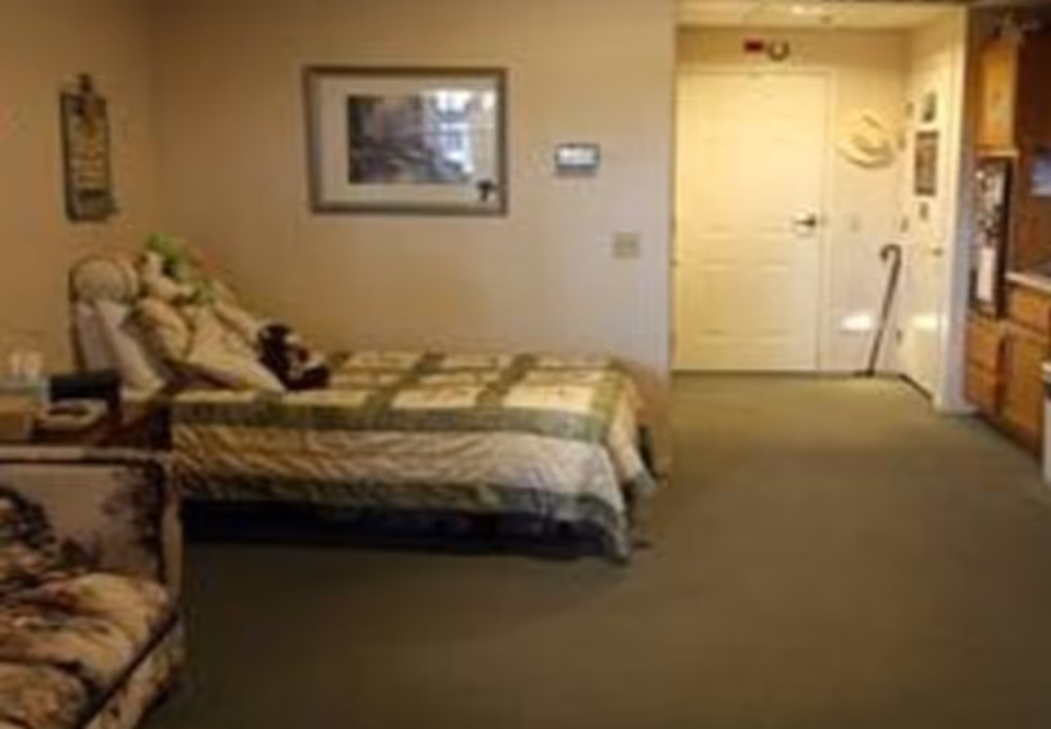 Studio-style bedroom with a single bed, armchair, framed wall art, and a door opening to a hallway.