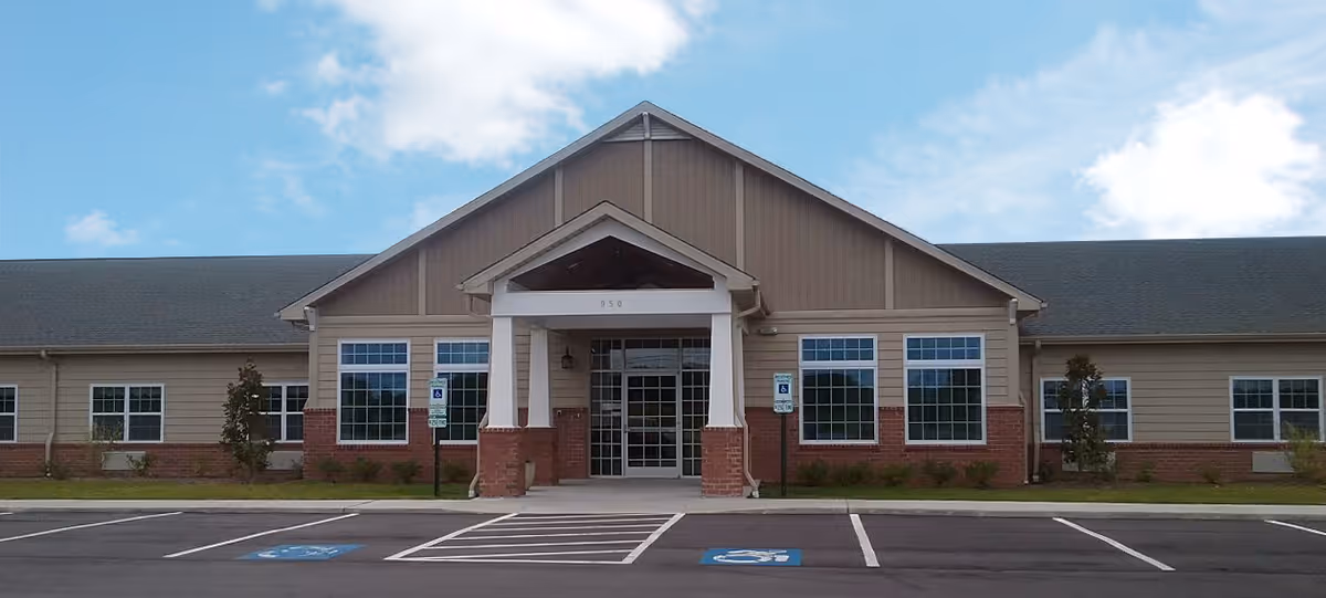 Front exterior view of Tyrrell House, a single-story building with a peaked roof, large windows, and a covered entrance supported by white columns. The parking lot in front includes designated handicapped parking spaces.