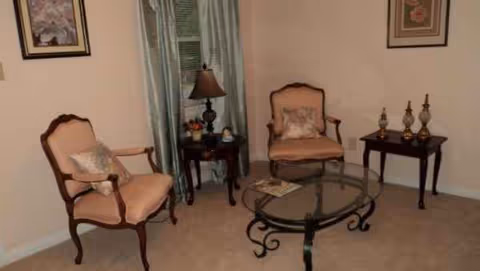 Cozy living room in a senior care home with two upholstered chairs, glass coffee table, lamps.