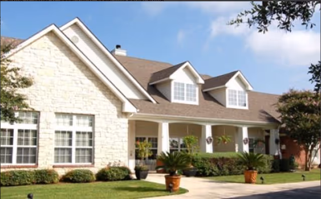 Front exterior of a single-story senior living building with a covered porch, dormer windows, and landscaped lawn.