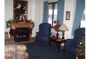 Interior living room with a fireplace, two blue armchairs, a floral sofa, a side table with lamp, and holiday decorations.