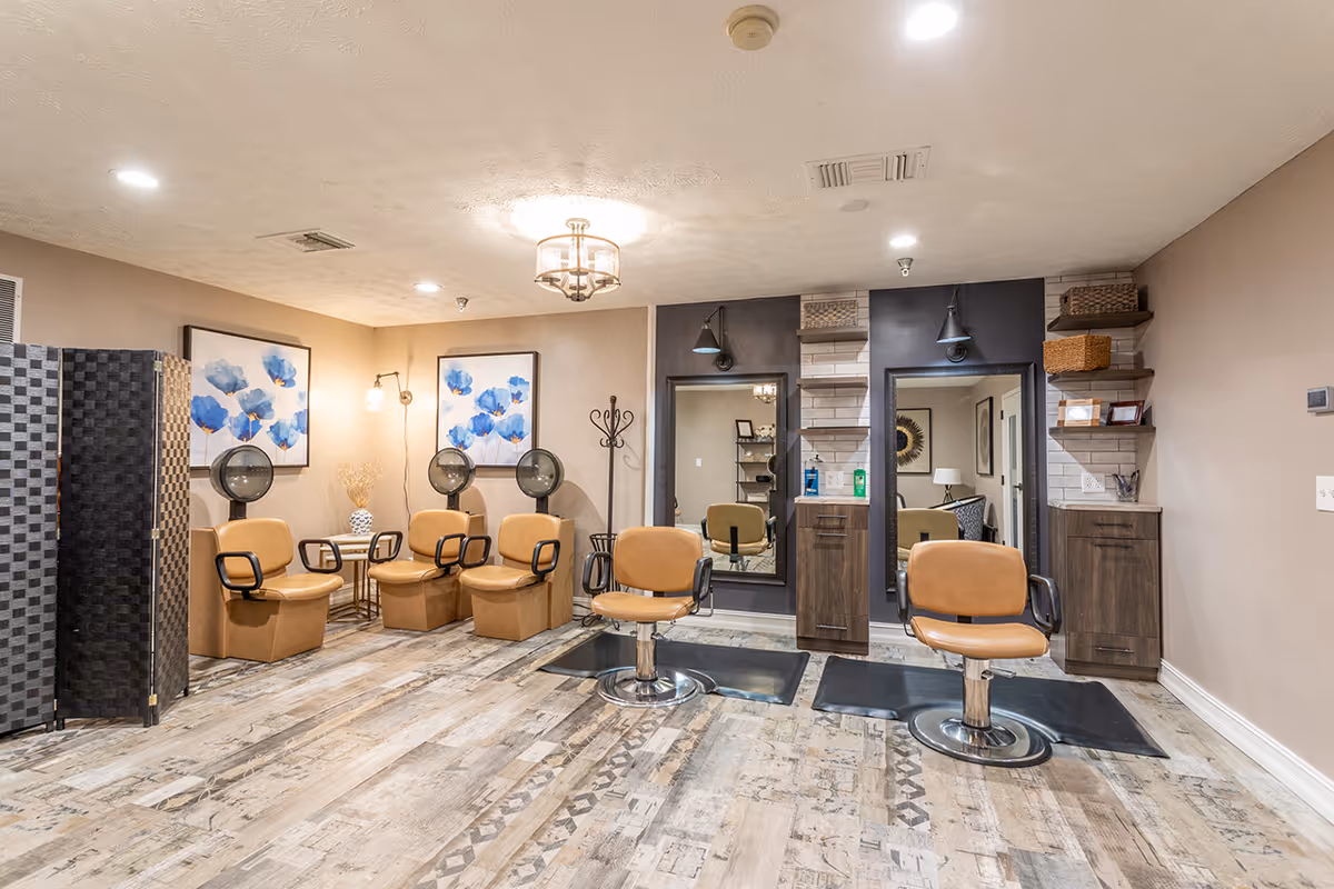 Interior salon area with styling chairs, hooded dryers, mirrors and artwork in a senior living facility.