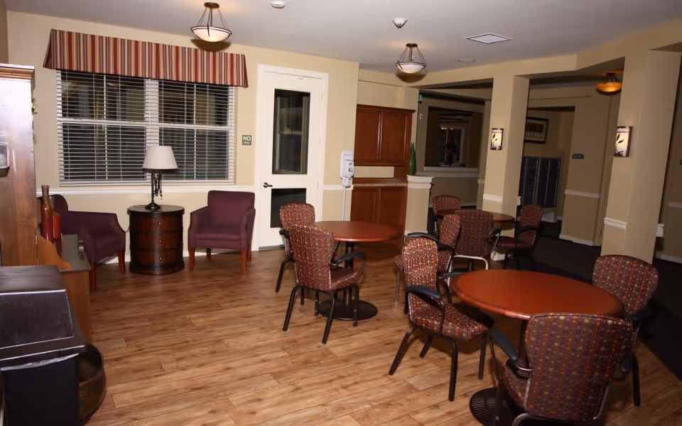 Common area with round dining tables and patterned chairs, a seating nook with two armchairs by a window, and wood-look floors.