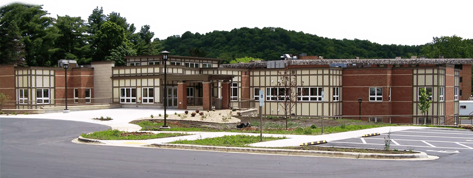 Front exterior of a single-story brick and beige senior living facility with a driveway, parking area, and landscaped grounds.