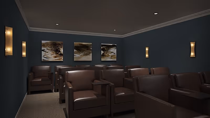 A small theater room with multiple rows of dark brown leather armchairs, each equipped with a small side table. The walls are painted dark blue and decorated with three abstract paintings on the back wall and modern wall sconces emitting warm light. The ceiling is dark with recessed lighting.
