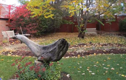 Outdoor courtyard with autumn leaves, a bird statue, trees, benches, and brick wall.