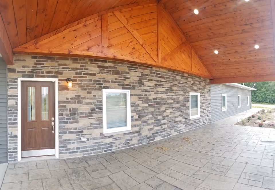Exterior of a facility with stone veneer, gray siding, and a wooden peaked roof overhang.