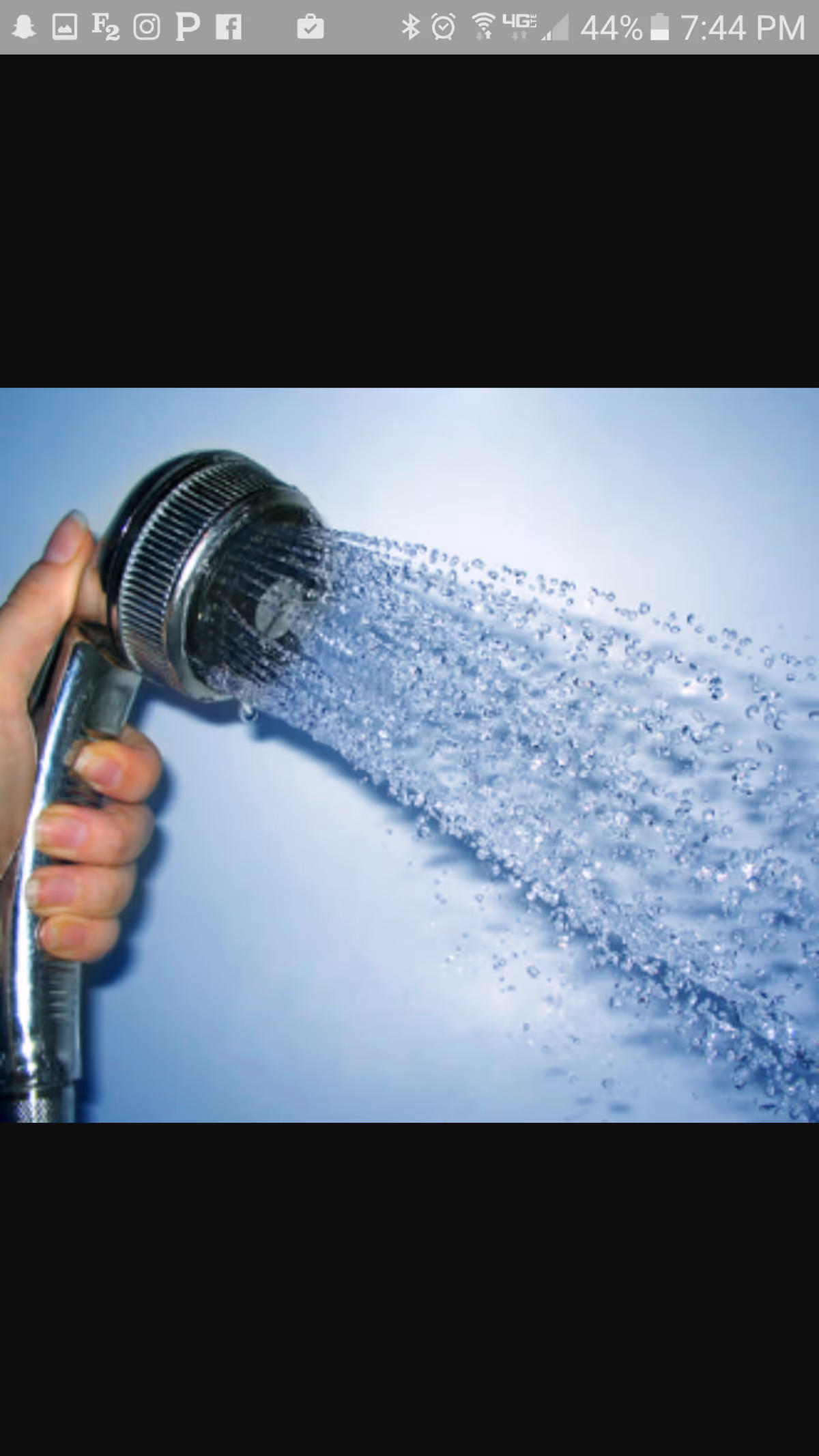 A hand holding a chrome shower head spraying a strong stream of water.