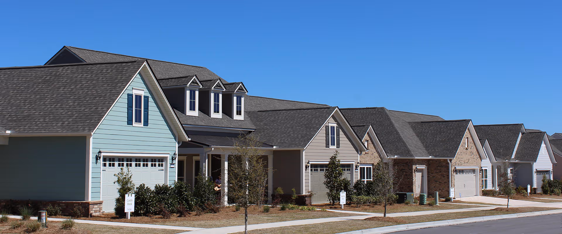 Row of modern single-family homes with garages and well-maintained landscaping under a clear blue sky in a residential neighborhood.