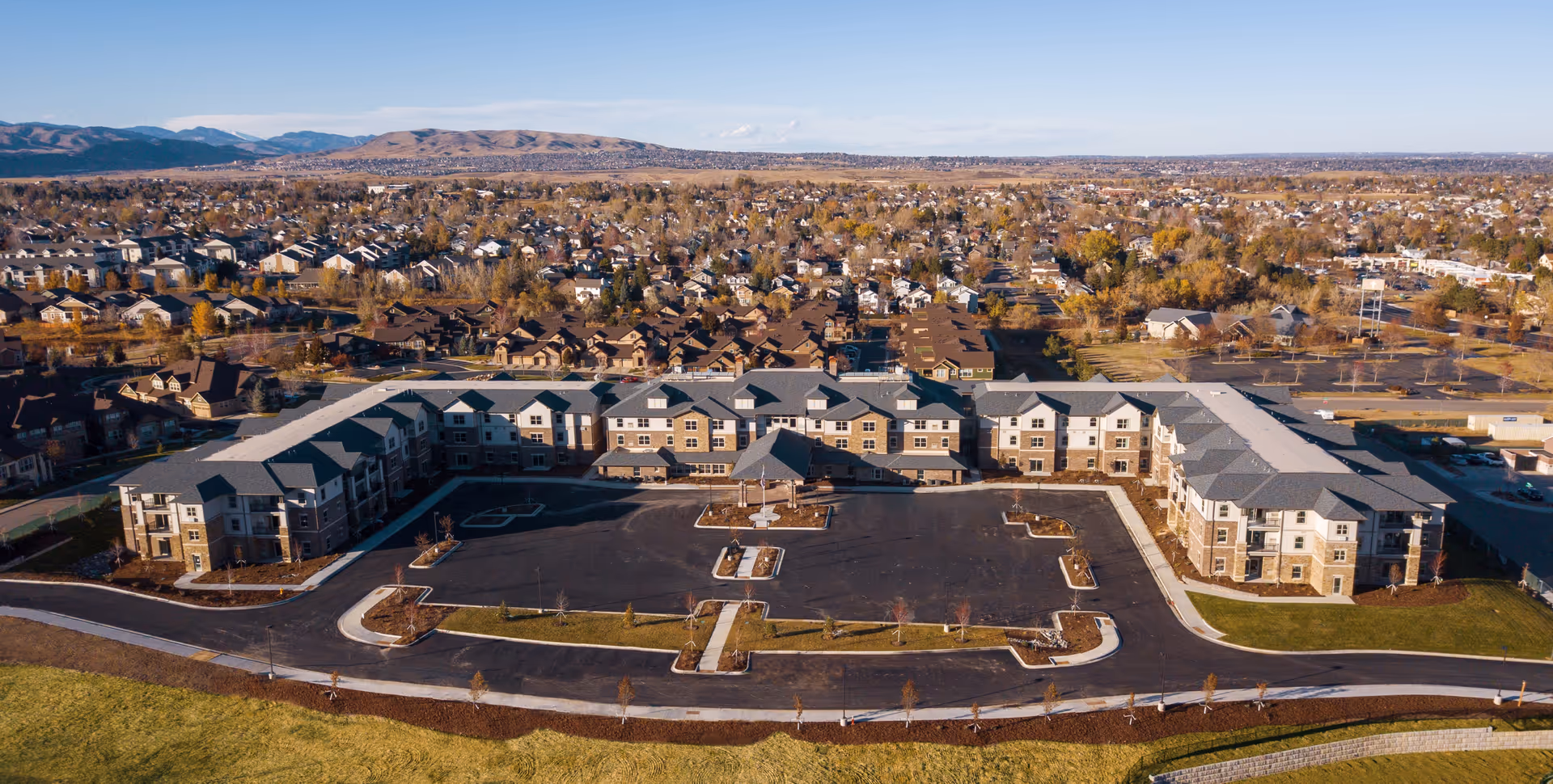 Aerial view of the Sky Pointe Retirement Resort complex with a large central parking area, landscaped grounds, surrounding neighborhood, and distant mountains.