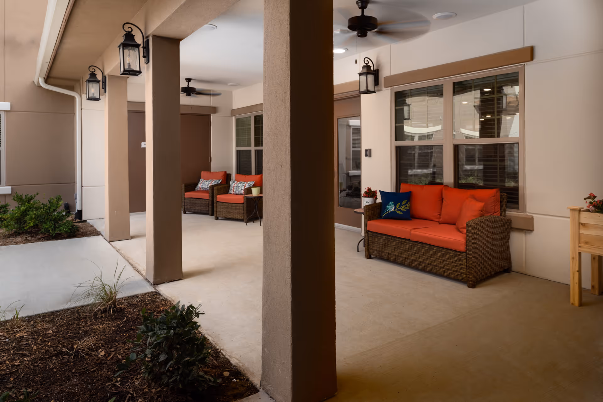 Covered outdoor patio with wicker seating and bright orange cushions along a shaded walkway.
