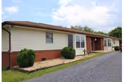 Single-story cream building with red brick accents, driveway, and trimmed shrubs.