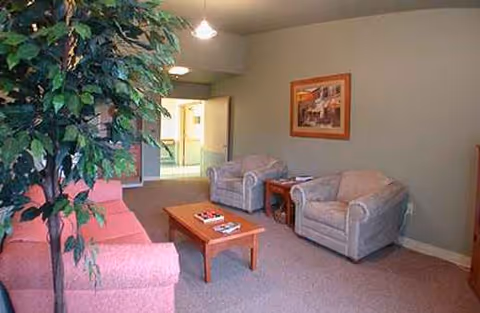 A waiting lounge with pink sofa, two armchairs, a coffee table, and a plant.