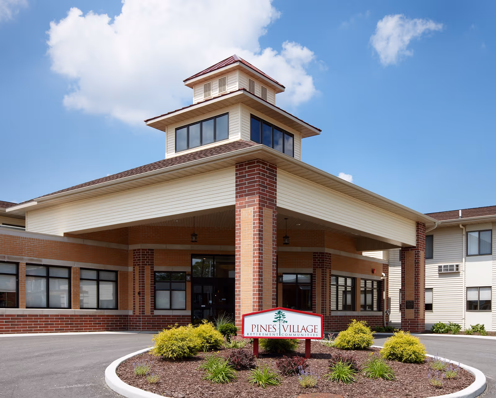 Exterior view of Pines Village retirement community entrance with sign and landscaping.