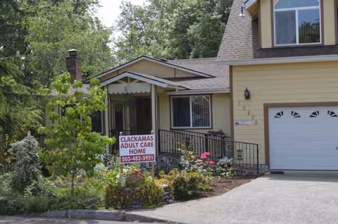 Exterior view of a house-style senior care home with a garden and front sign.