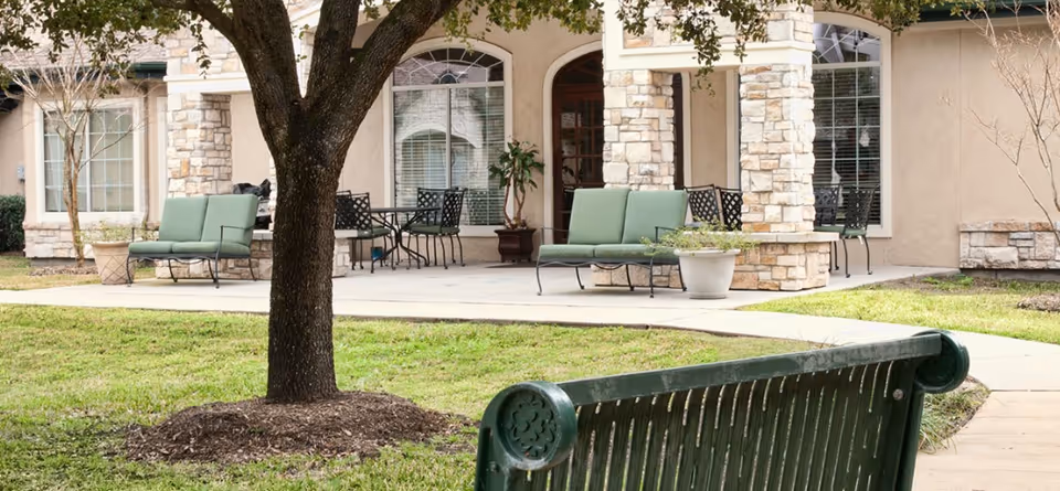 Outdoor patio area with green benches, a tree, potted plants, and a stone-accented building façade.