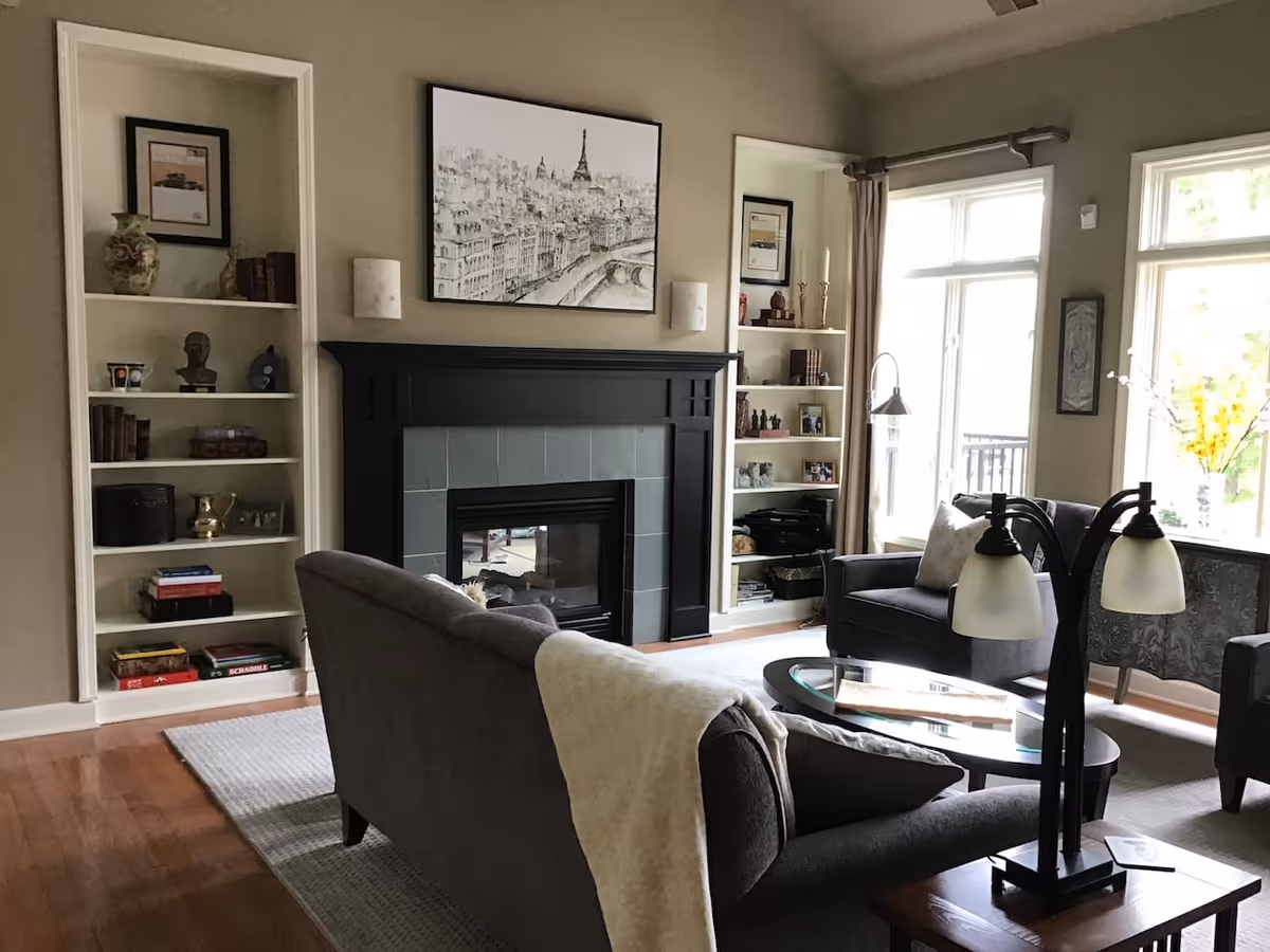 Bright living room with a fireplace, built-in bookshelves, sofas, a coffee table, and large windows.