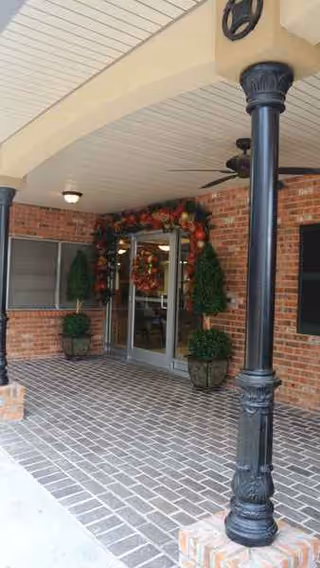 Brick entryway with glass doors, wreaths, potted plants, and decorative columns under a covered porch.