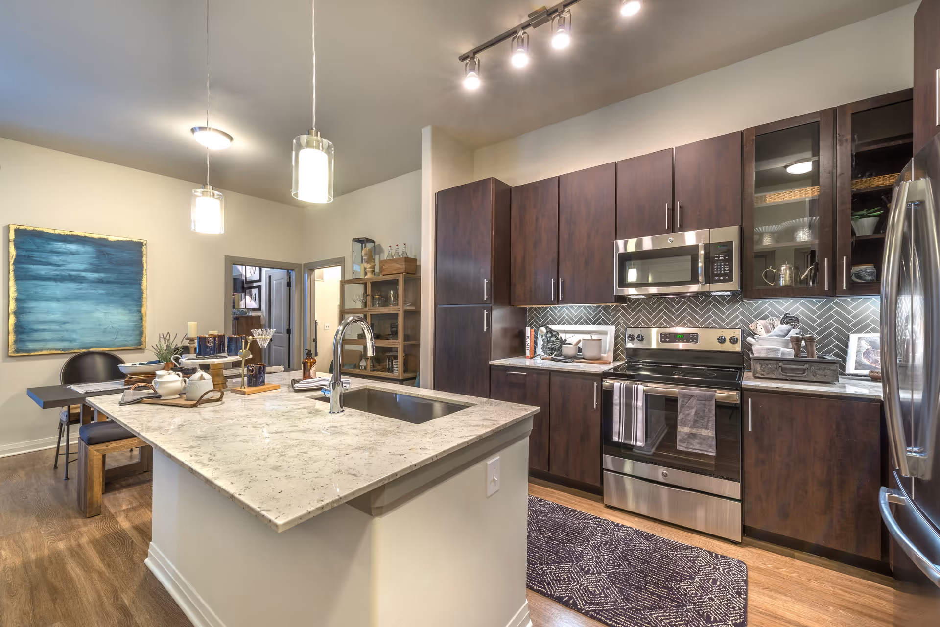 Modern kitchen with a marble island, stainless steel appliances, dark wood cabinets, pendant lights, and an adjacent dining area.