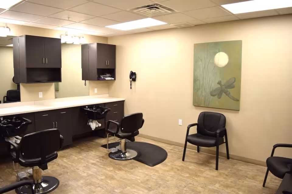 Interior salon area with styling chairs, shampoo sinks, a long countertop with cabinets and a small seating area with wall art.