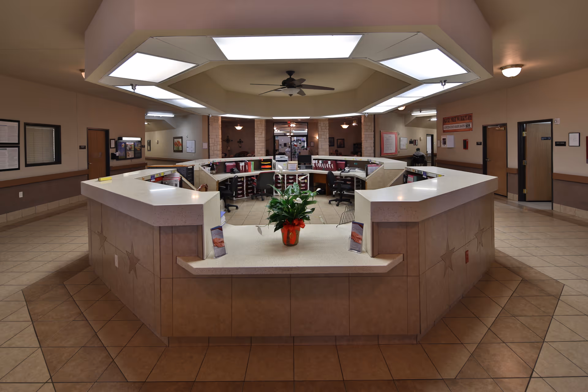 Central nurses' station reception desk in a nursing home lobby with a potted plant on the counter.