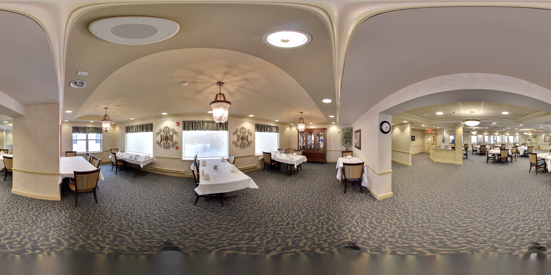 Spacious carpeted dining room with multiple set tables and chairs, chandeliers, and decorative wall accents.
