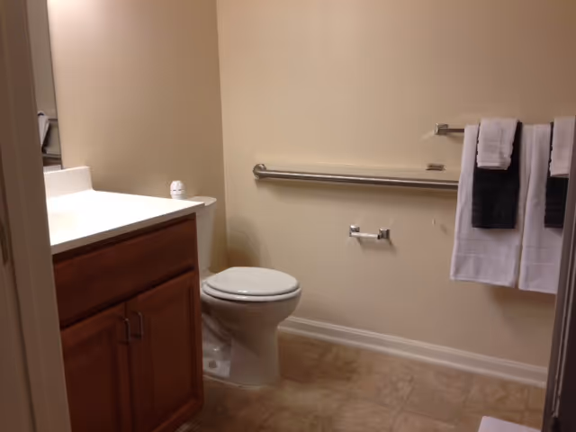 Bathroom in a senior living facility with sink, toilet, and towel bars.