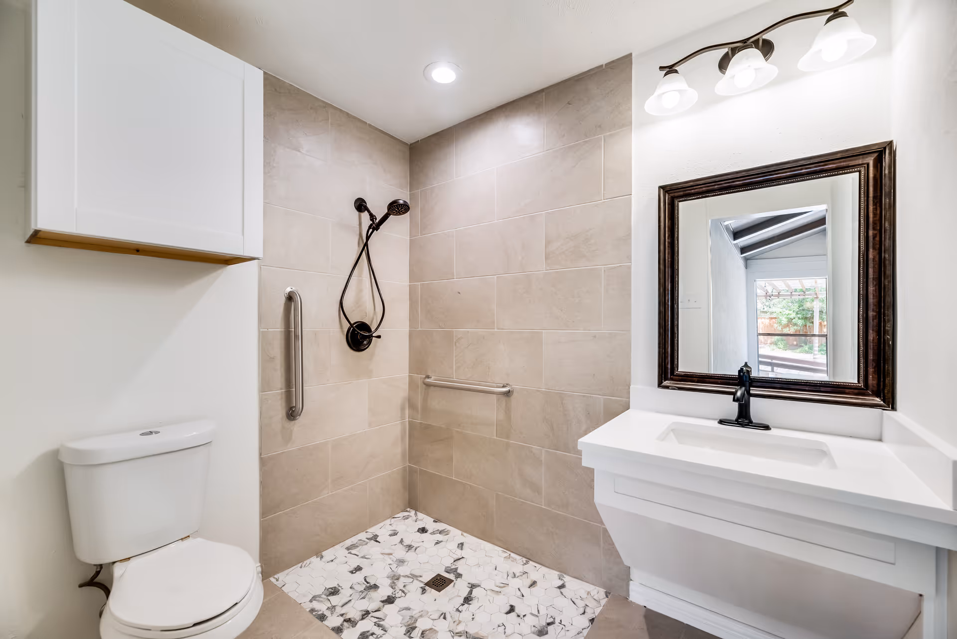 Accessible bathroom with a tiled walk-in shower, toilet, and vanity with mirror and light fixture.