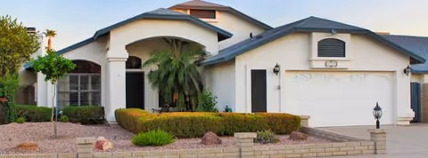 A single-story senior living facility with arched entrance, columns, palm trees, and desert landscaping.
