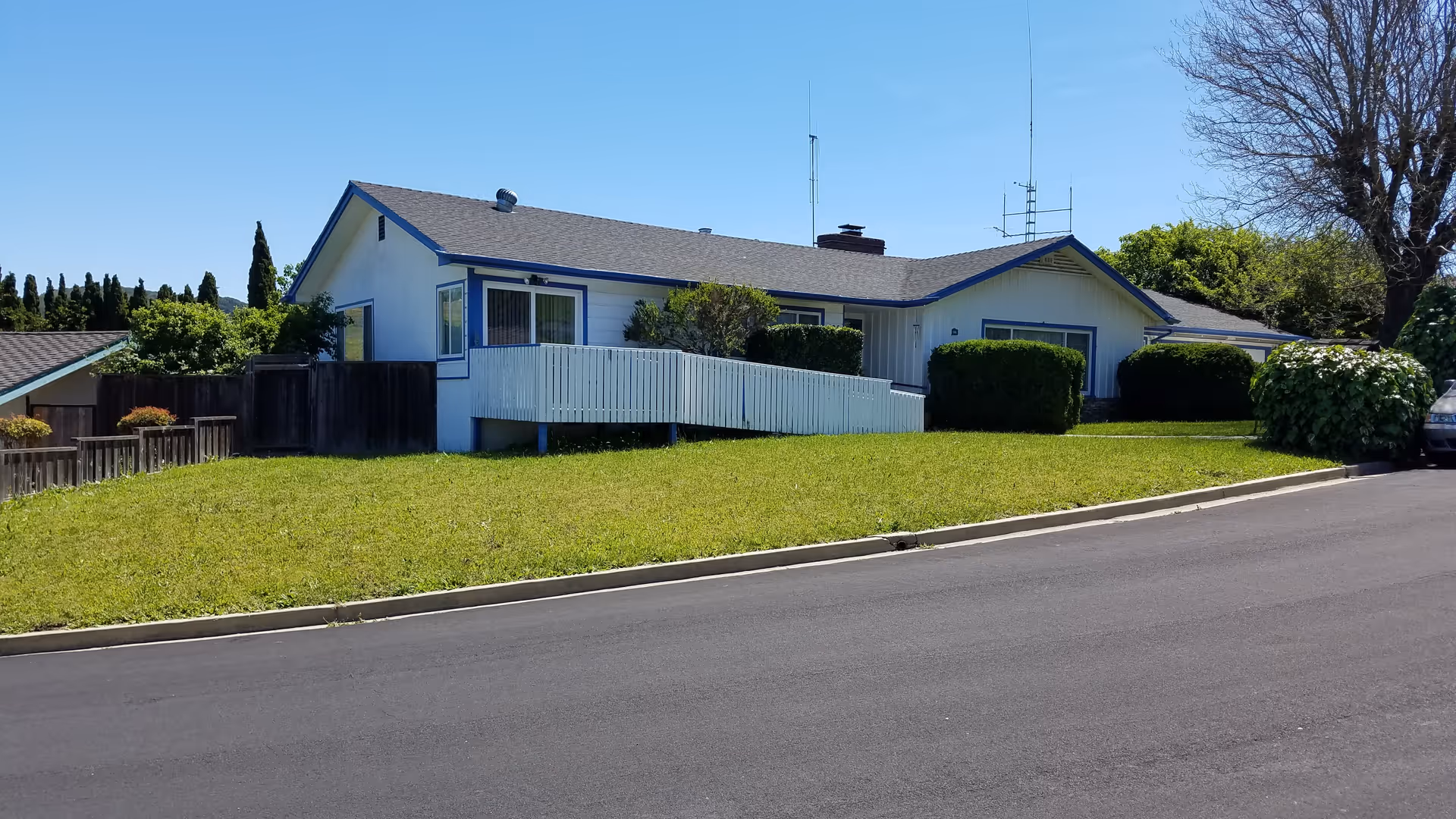 Single-story light-colored house with a front wheelchair ramp and a grassy lawn on a sunny day.