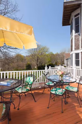 Outdoor balcony patio at Royal at Harwich with a glass table, chairs, and a yellow umbrella.