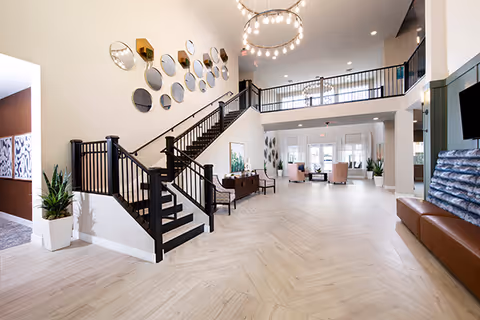 Spacious modern lobby with a central staircase, chandelier, and seating area.