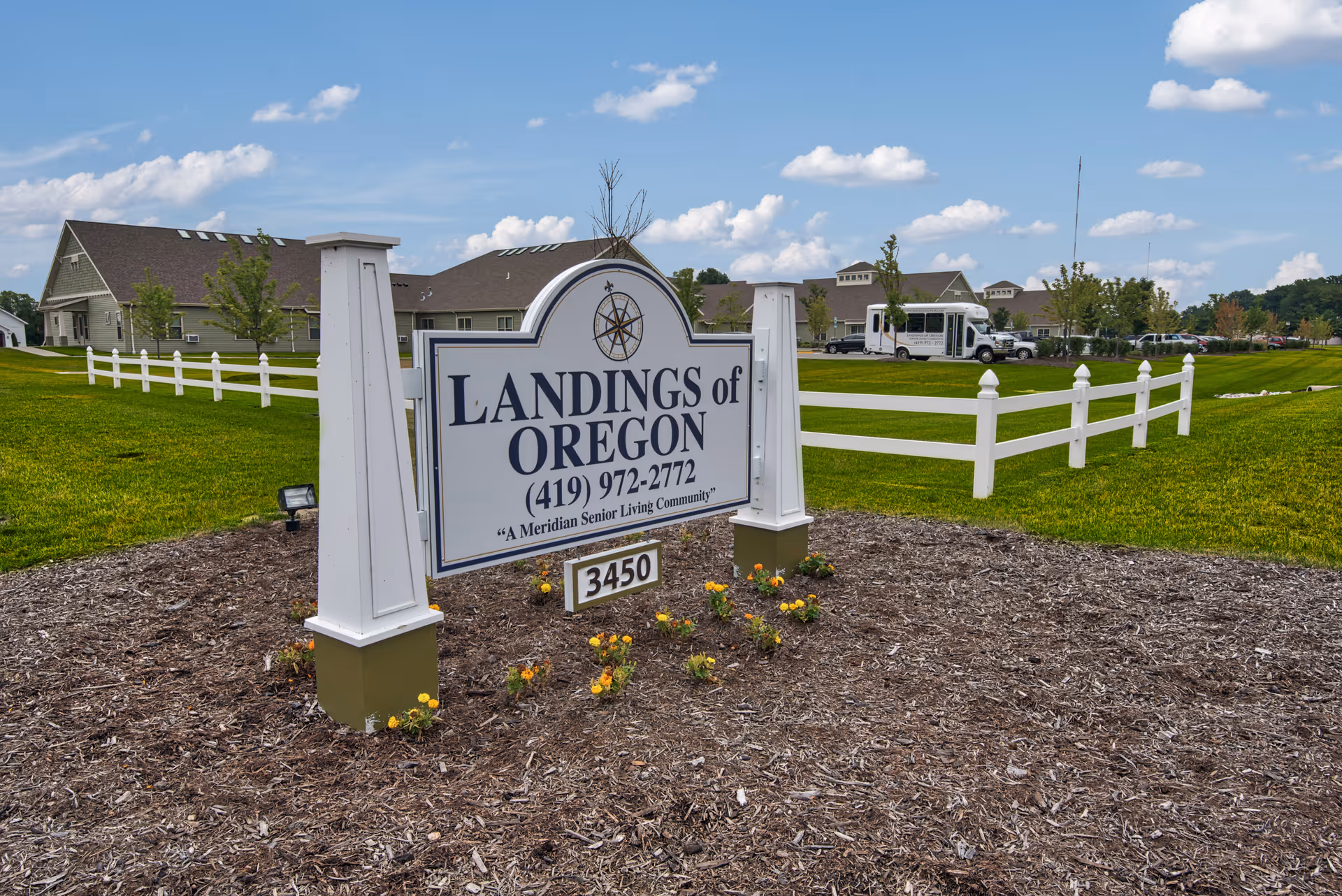 A large sign reading "Landings of Oregon" sits on a landscaped lawn with a white fence and senior living buildings in the background.