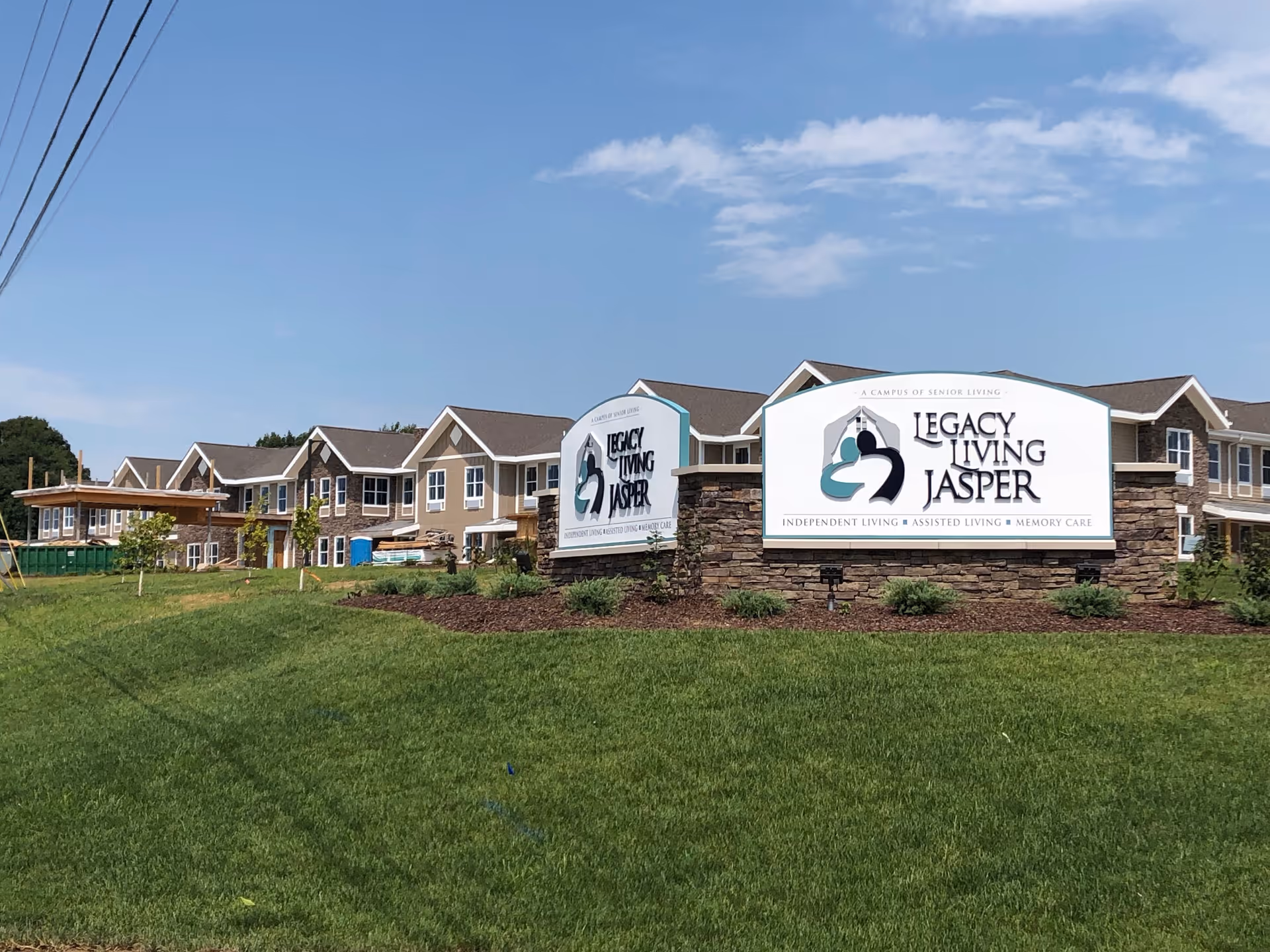 Exterior view of the Legacy Living Jasper senior living complex with large stone signs on a grassy lawn and the building behind them.