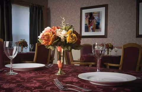 A formal dining room in Pleasant Ridge Healthcare Center with burgundy tablecloths and flowers.