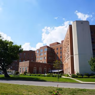 Brick senior living facility exterior with manicured lawn and blue sky.
