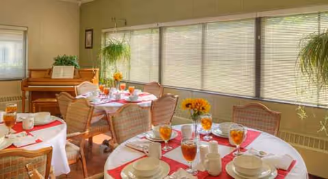 A bright dining room with round tables, place settings, and large windows.