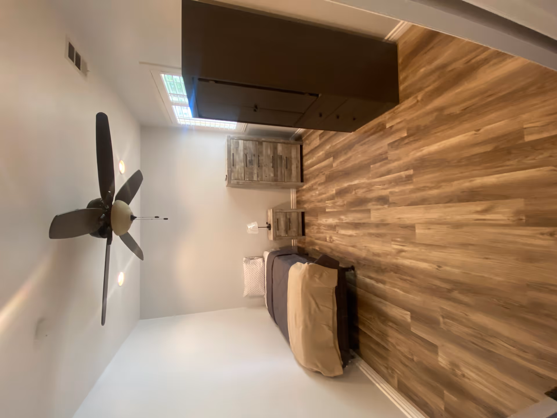 Simple bedroom with a single bed, wooden dressers and nightstand, a ceiling fan, and wood-look flooring.