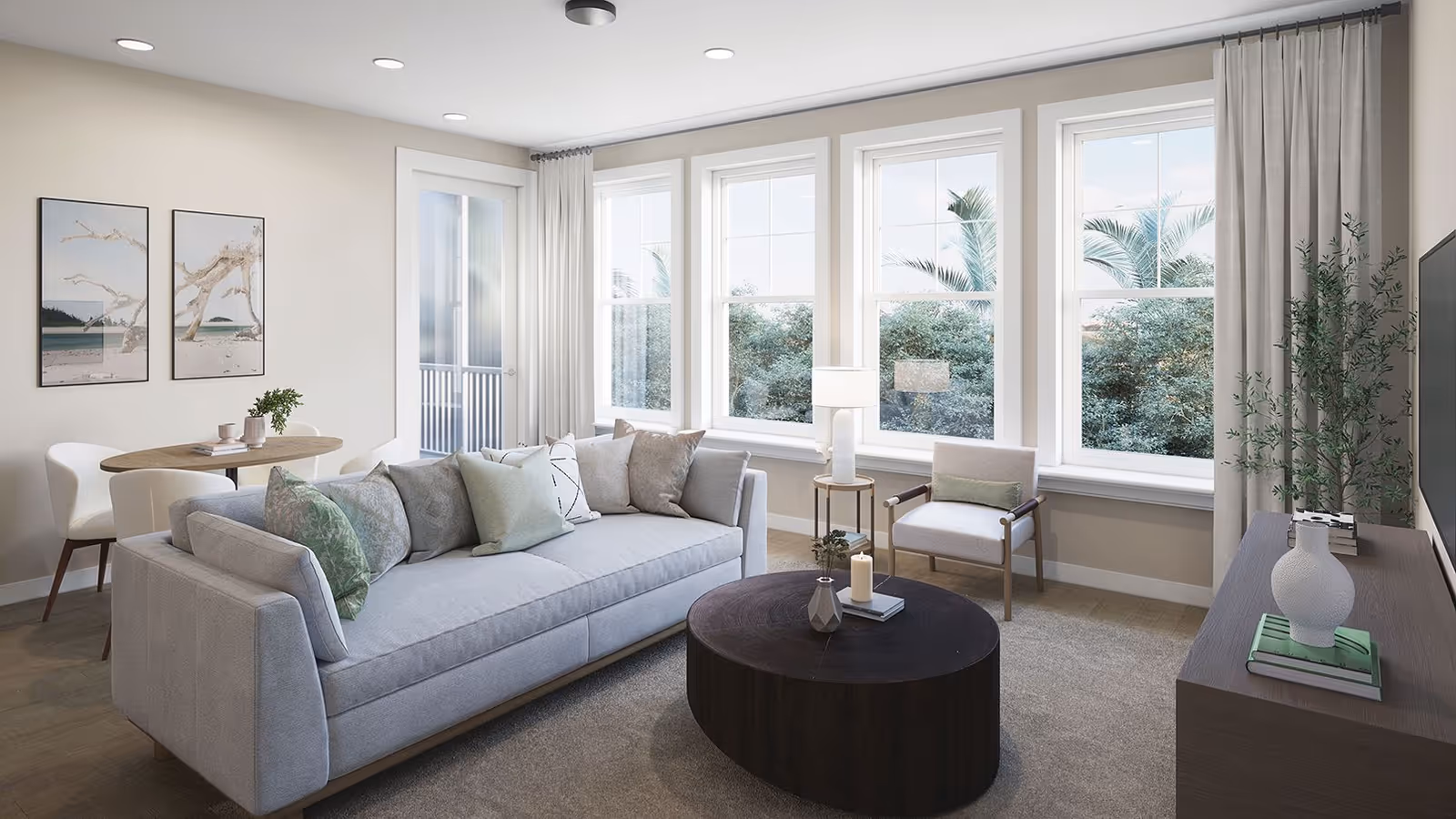 Bright modern living room with a sofa, round coffee table, armchair, large windows, and a small dining area.