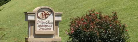 Willow Ridge Rehabilitation & Living Center sign on a grassy slope with red shrubs.