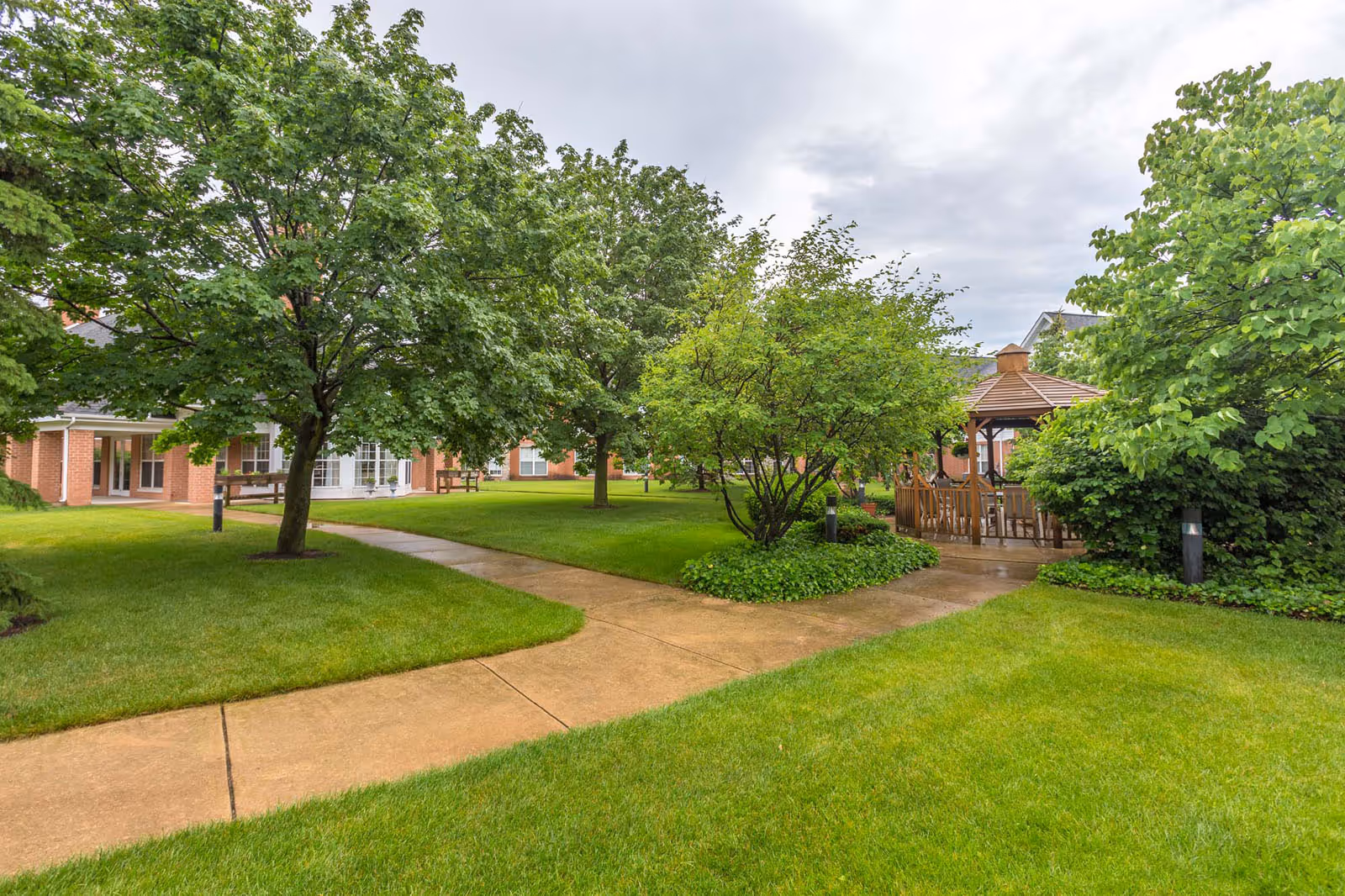 Well-maintained grassy courtyard with paved walkways, trees, a gazebo, and a brick building in the background.