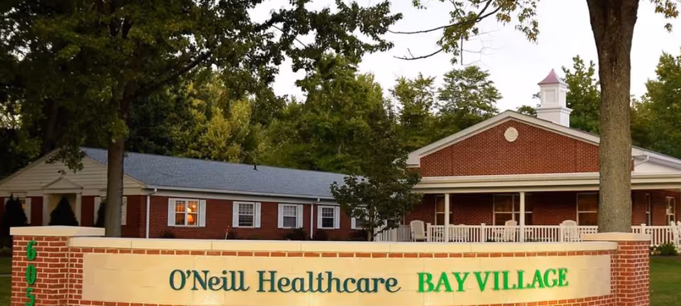 Brick senior healthcare building with a front sign reading "O'Neill Healthcare BAY VILLAGE," trees, and a porch.