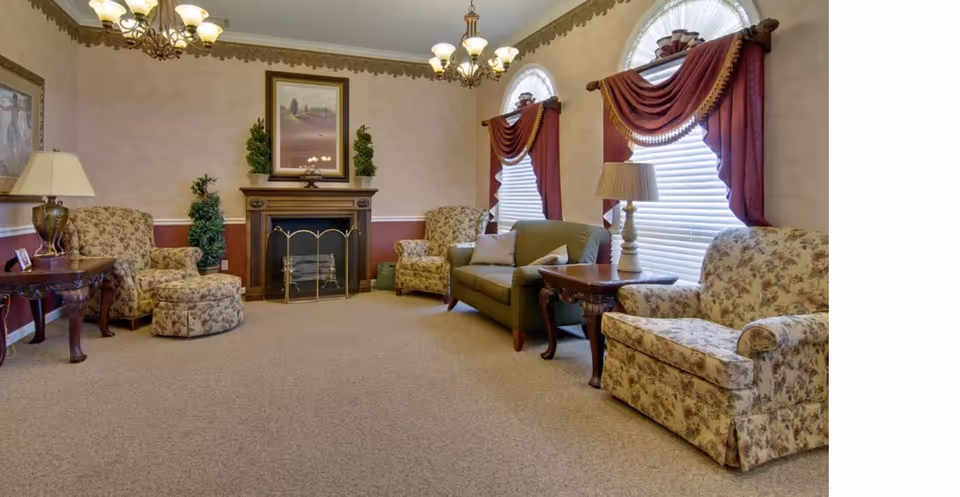 Comfortable sitting room with floral armchairs, a sofa, fireplace, and draped arched windows.